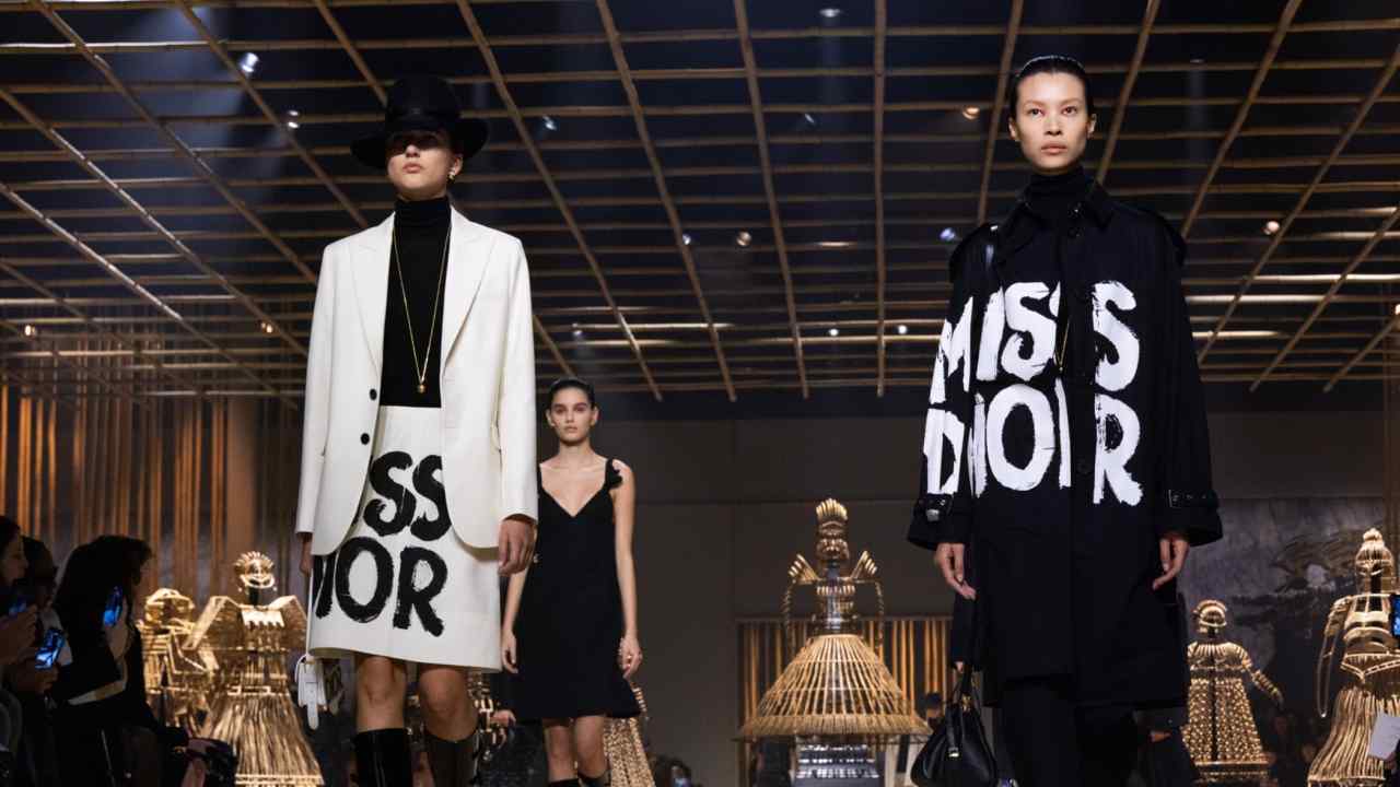 Models wear black and white suits and coats emblazoned with the words Miss Dior in brushstroke style