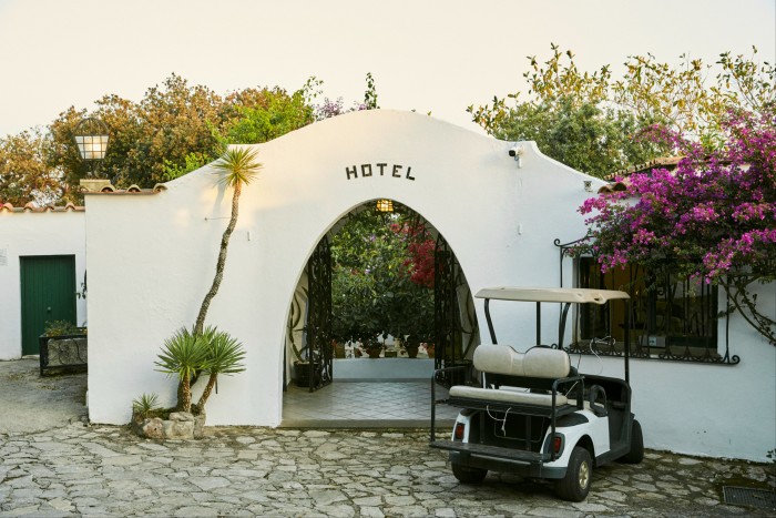 The white-stucco-arch entrance to Hotel Punta Rossa, with a golf buggy to the right and bougainvillea flowering over the walls