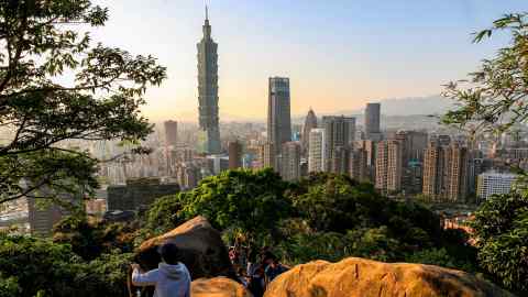 People climb a hill to enjoy a view of the Taipei 101 megatall skyscraper in Taipei, Taiwan