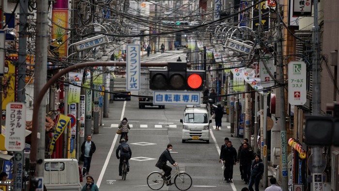 Pedestrians, bicyclists and traffic pass under power lines in a city in Tokyo, Japan