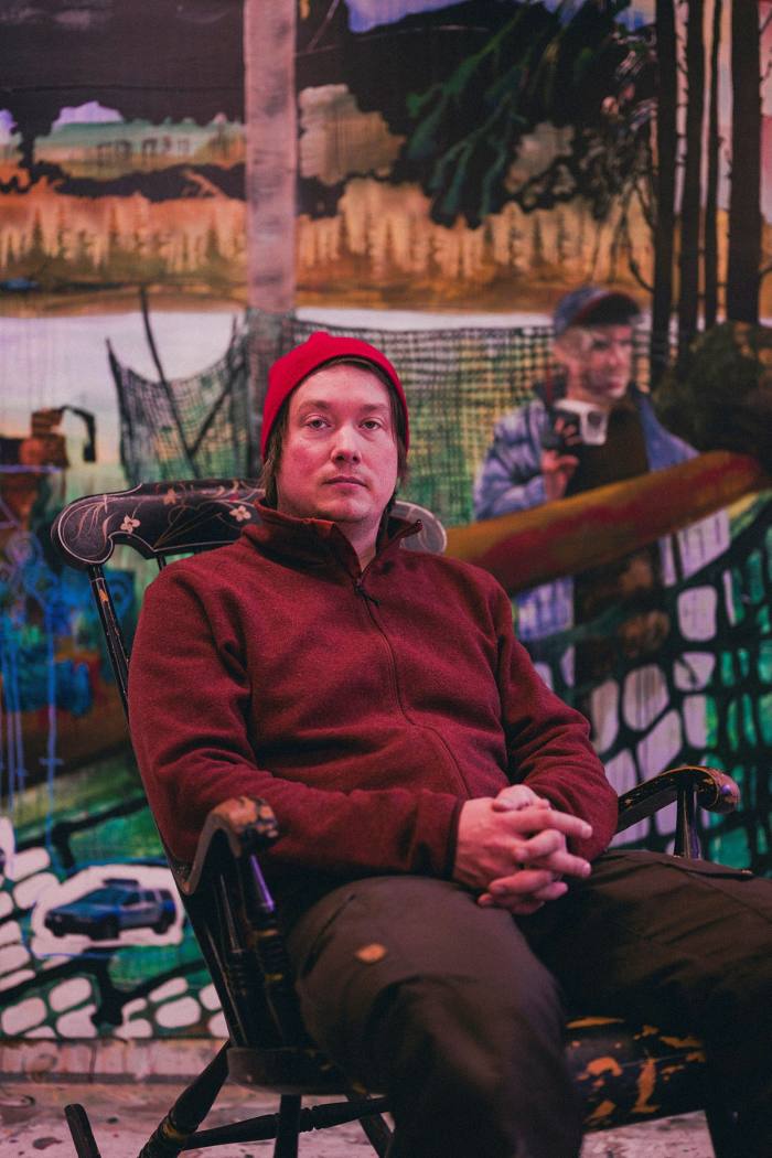 Artist Anders Sunna in fleece top and woolly hat sits and stares into the camera