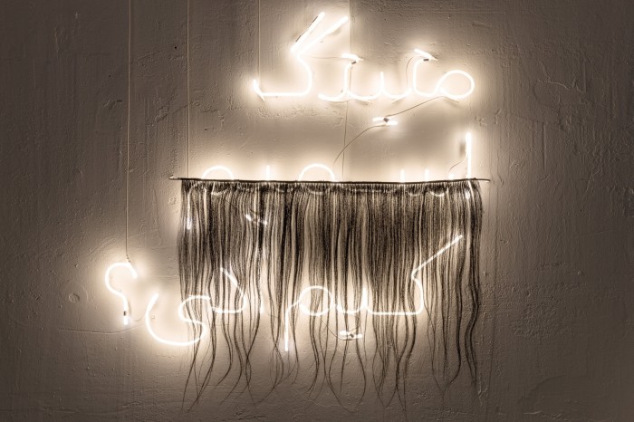 Arabic writing in white neon with a hairy curtain partially over it