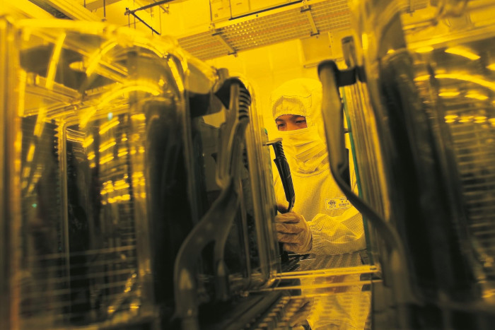 A chip engineer wearing a clean room suit works with chip manufacturing equipment