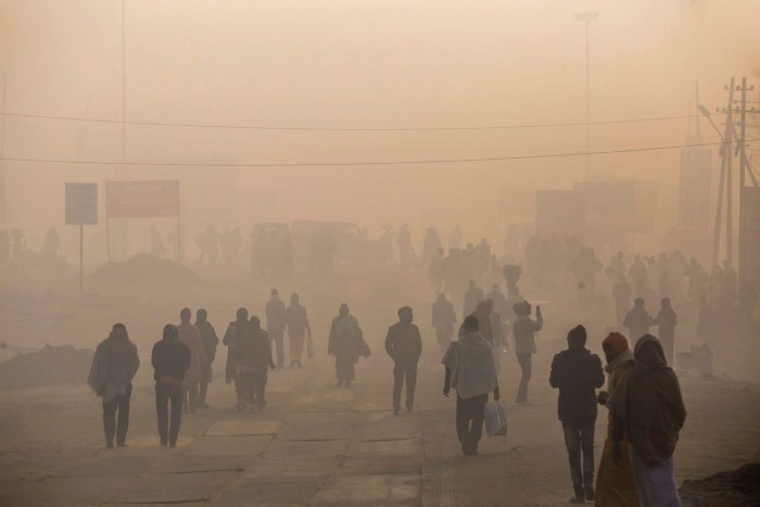 Pedestrians walk along a road shrouded in smog as they arrive for the Kumbh Mela religious festival in Prayagraj, Uttar Pradesh