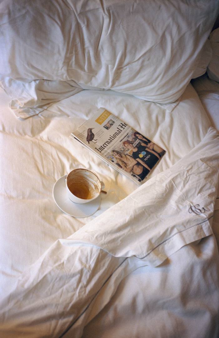 An empty coffee cup and a newspaper on an unmade bed