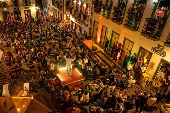 A large crowd gather in a square lit at night, listening to and dancing to music 