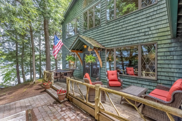 Chairs and an American flag adorn a deck outside a green wooden home