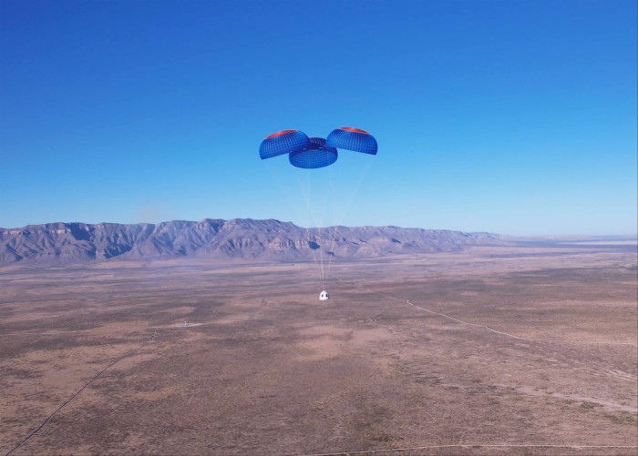 A space capsule carried by parachutes floats down to an empty flat landscape