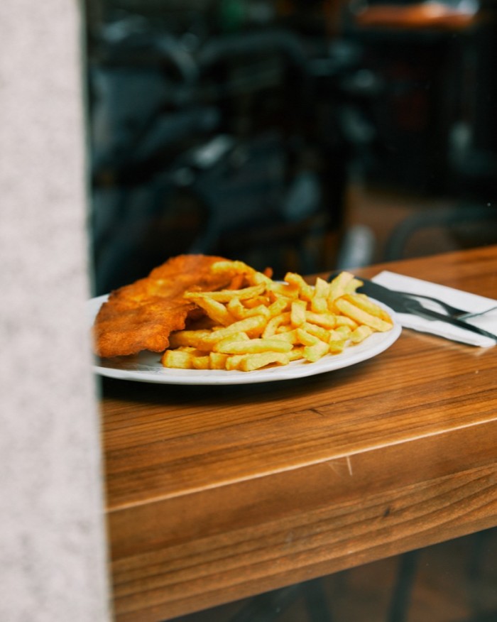 A plate of escalope and chips on a wooden counter at Casa Dani