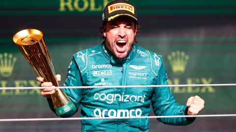 Aston Martin driver Fernando Alonso on the podium holding a trophy, looking so pumped up for getting a podium finish