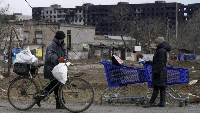 A man wheels a bicycle past woman standing with her belongings in two shopping trolleys
