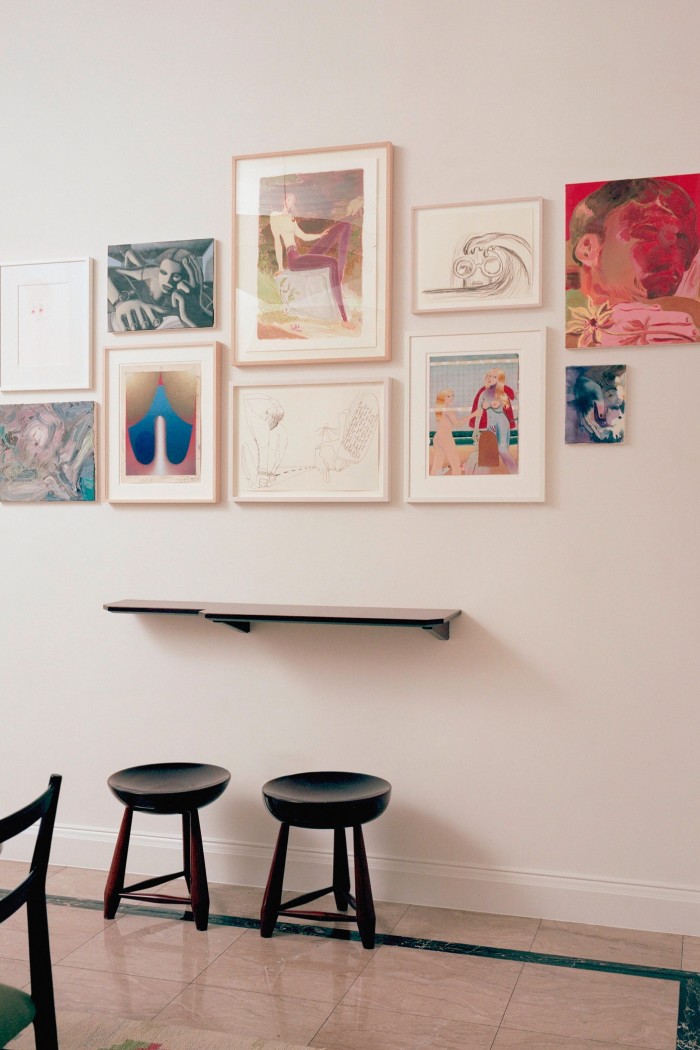 A pair of black stools stand against a cream-coloured wall where several paintings hang