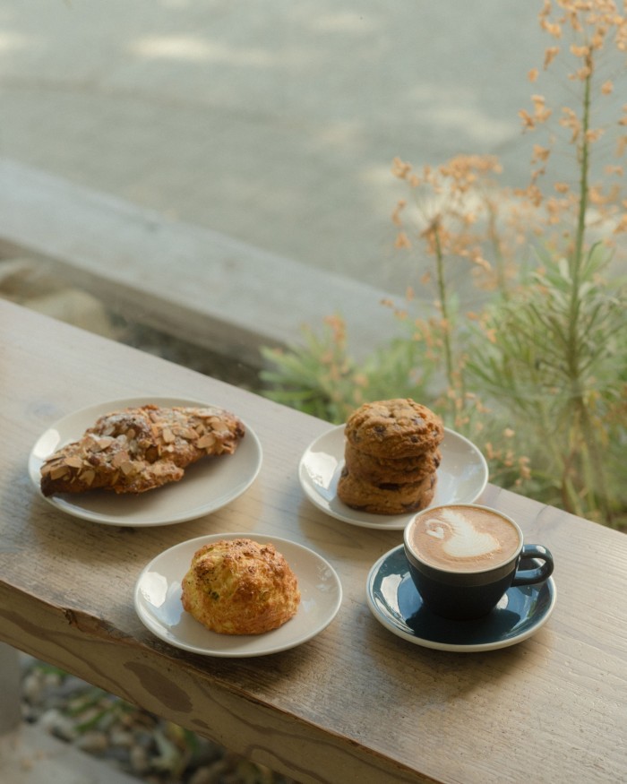 A cup of coffee and three plates of baked goods on a wooden counter at Elysian