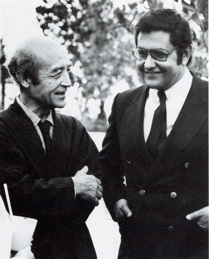 Two men in suits chat in a black and white photo 