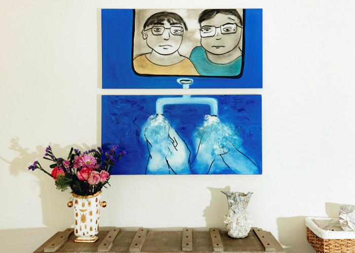 Photo of a painting on a domestic wall. The painting shows two people looking out and below two people washing their hands. There is a table with a vase of flowers below
