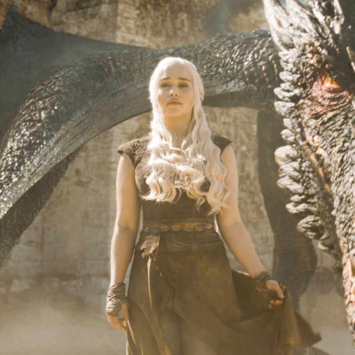 A woman with long white-blonde hair stands proudly in front of a dragon 