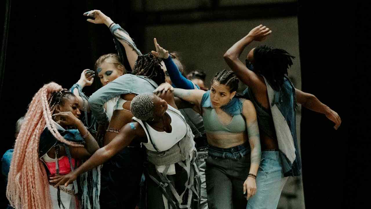 A group of dancers form a cluster, extending their arms and twisting their bodies