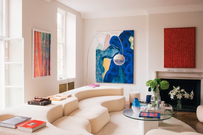 A bright white living room with a double-semicircular cream sofa and bright paintings on the wall