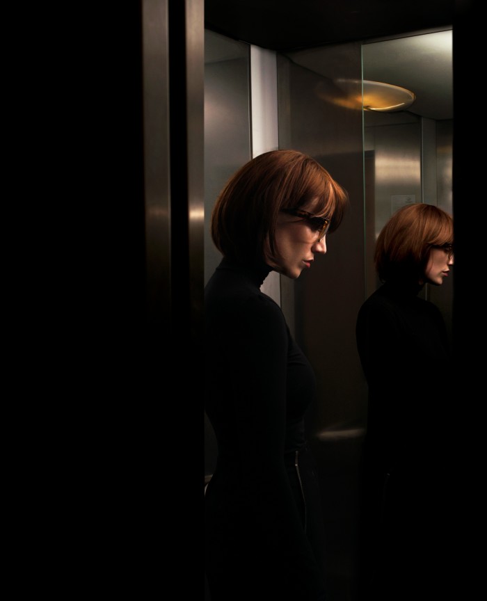 Woman wearing glasses and a black, turtle neck outfit inside an elevator