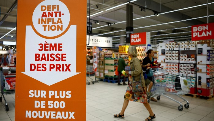 A sign reading ‘Anti-inflation challenge, third price cut on more than 500 new products’ is seen as customers shop at a Carrefour supermarket near Paris