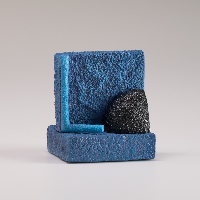 Two rough blue ceramic squares perpendicular to each other with a black lump