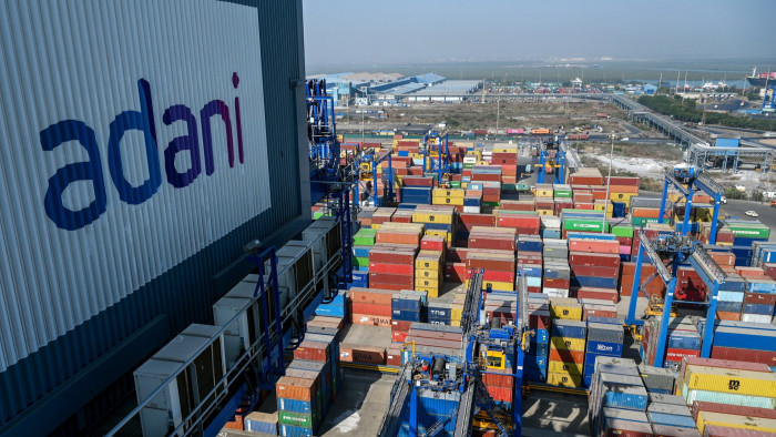 A general view of the Adani-owned Mundra Port with the Adani logo in the foreground on a giant billboard and shipping containers in the background