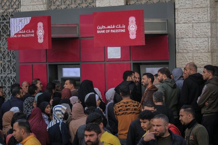 Palestinian public sector employees crowd around automated teller machines 