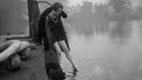 A bather, still wearing her fur coat, tests the water at one of Hampstead Heath’s ponds, c1930
