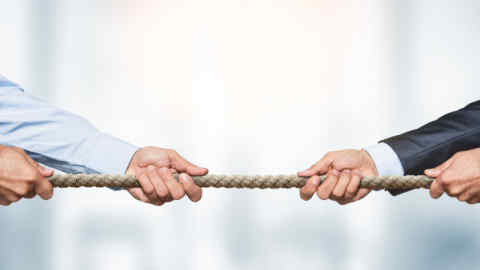 Tug of war, two businessman pulling a rope in opposite directions over defocused background with copy space