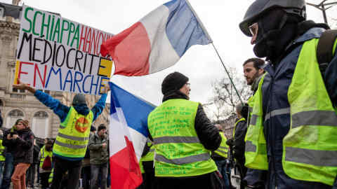 Demonstrators wearing yellow vests (Gilets jaunes) wave French national flags during protests on the Champs-Elysees in Paris, France on Saturday, Jan. 26, 2019. French President Emmanuel Macron plans changes in the staff at the Elysee Palace following months of protests from the Yellow Vests movement, Le Parisien reported, citing government officials it didn’t name. Photographer: Anita Pouchard Serra/Bloomberg