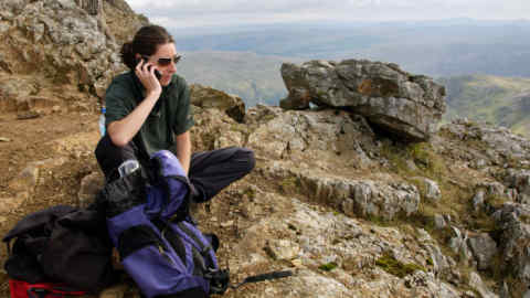 AGEEB7 Young woman using a mobile phone on rock ledge while walking on Crib Goch in Snowdonia Gwynedd North Wales UK