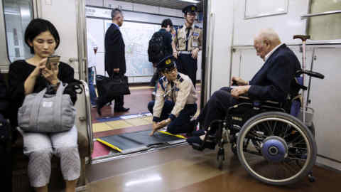 Subway employees help an elderly man in a wheelchair to disembark from the train at a station in Tokyo on May 8, 2017. / AFP PHOTO / Behrouz MEHRI (Photo credit should read BEHROUZ MEHRI/AFP/Getty Images)
