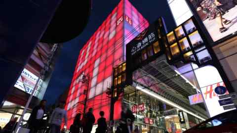 Shoppers and pedestrians walk past the Fast Retailing Co. Uniqlo flagship store illuminated at night in Osaka, Japan, on Wednesday, April 11, 2018. Fast Retailing's half-year earnings figures are scheduled to be released on April 12. Photographer: Buddhika Weerasinghe/Bloombergg