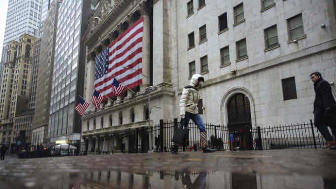 A pedestrian wearing a surgical mask and gloves walks past the New York Stock Exchange on Thursday, March 19, 2020, in New York. Stocks are swinging between gains and losses in early trading on Wall Street Thursday, but the moves are more subdued than the wild jabs that have dominated recent weeks. At least for now. (AP Photo/Kevin Hagen)
