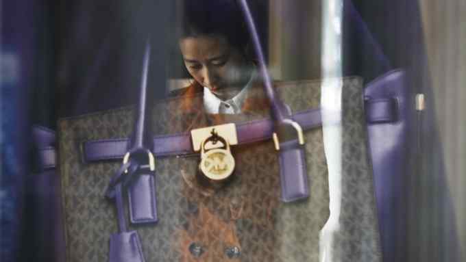 A luxury purse is reflected on a woman checking on her smartphone outside a fashion boutique at a popular shopping mall in Beijing, on Thursday, Oct. 19, 2017. China's economic growth edged down in the latest quarter but was buoyed by strength in retail spending and exports. (AP Photo/Andy Wong)