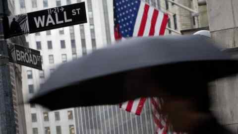 A pedestrian carrying an umbrella passes a U.S. flag on Wall Street in front of the exterior of the New York Stock Exchange (NYSE) in New York, U.S. Photographer: Scott Eells/Bloomberg