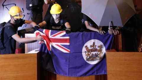 Protesters put a Hong Kong colonial flag and deface the Hong Kong logo at the Legislative Chamber after break in to protest against the extradition bill in Hong Kong, Monday, July 1, 2019. The extradition law has aroused concerns that this legislation would undermine the city's independent judicial system as it allows Hong Kong to hand over fugitives to the jurisdictions that the city doesn't currently have an extradition agreement with, including mainland China, where a fair trial might not be guaranteed. (AP Photo/Vincent Yu)