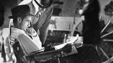 Millionaire Howard Hughes/movie studio owner (L) studying script as he sits, conferring w. undent. man, on the movie set for the Outlaw. (Photo by Bob Landry/The LIFE Picture Collection/Getty Images)