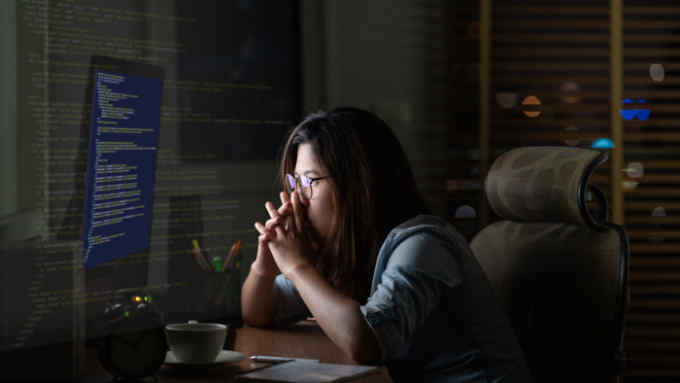 Portrait of Asian Businesswoman sitting and working hard on the table with front of computer desktop with programming source code over computer screen in work place at late with serious action