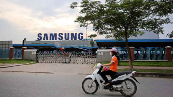A motorcyclist rides past the Samsung Electronics Vietnam Co. Plant at Yen Phong Industrial Park in Bac Ninh Province, Vietnam, on Thursday, Sept. 1, 2016. Samsung Electronics Co. and its affiliate have built a factory town with 45,000 young workers and hundreds of foreign component suppliers -- a miniature version of the family-run chaebol conglomerates that dominate business back in Korea. The investment has been a windfall for businesses in Bac Ninh -- almost 2,000 new hotels and restaurants opened between 2011 and 2015 according to the provincial statistics office -- helping raise the province's per capita GDP to three times the national average. Photographer: Linh Luong Thai/Bloomberg