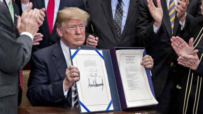 U.S. President Donald Trump, center, holds up S. 2155, the Economic Growth, Regulatory Relief, And Consumer Protection Act, after being signed with administration officials and members of Congress in the Roosevelt Room of the White House in Washington, D.C., U.S., on Thursday, May 24, 2018. The House Tuesday voted 258-to-159 to send Trump the most significant overhaul of banking oversight to become law since Dodd-Frank was enacted in 2010. Photographer: Andrew Harrer/Bloomberg