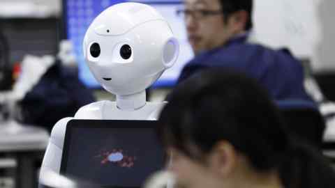 Pepper the humanoid robot, manufactured by SoftBank Group Corp., stands as employees work in the Orange Arch Inc. offices in Tokyo, Japan, on Monday, Oct. 5, 2015. Robots are everywhere. There are already 1.6 million of them, an army of disembodied limbs working in our factories to make everything from cars to pancakes. Now billionaire Masayoshi Son, chairman and chief executive officer of SoftBank, wants to bring robots into our homes. Photographer: Tomohiro Ohsumi/Bloomberg