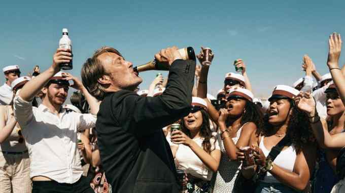 A scene from the 2020 Danish film ‘Another Round’ in which a man is drinking from a champagne bottle while a crowd of young people cheer him on