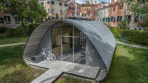 A grey concrete shelter with an arched roof and glass doors, with a bike parked in front