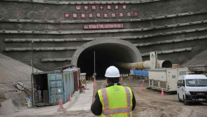 A worker stands near the entrance of a tunnel at a construction site