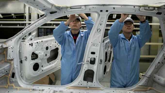Workers labor on vehicle bodies on the production line of a manufacturing plant