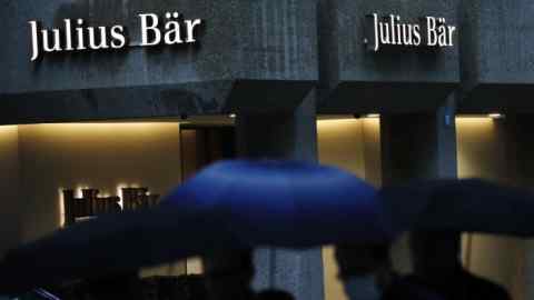 Pedestrians sheltering under umbrellas pass a Julius Baer Group branch in Zurich