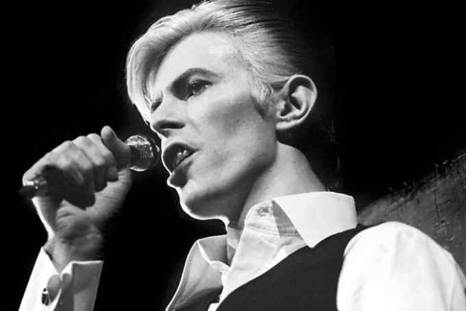 Dressed in a white shirt and black waistcoat, David Bowie sings into a microphone