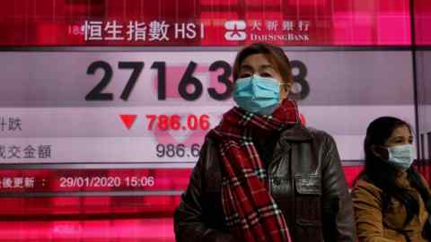 A woman wearing a face mask walks past a bank's electronic board showing the Hong Kong share index at the Hong Kong Stock Exchange in January