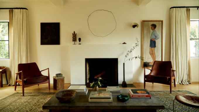 The living room, with its midcentury Ib Kofod-Larsen Seal chairs and antique Bibikabad rug. On the wall (from left) are Bureaucrat with Muted Tones, 2008, by British artist Charlie Hammond; a 1940s Japanese “tramp art” iron circle; a 1953 Serge Mouille sconce; and a 1931 portrait by Swedish artist Owe Zerge. On the hearth is a Rick Owens bronze swan-neck vase